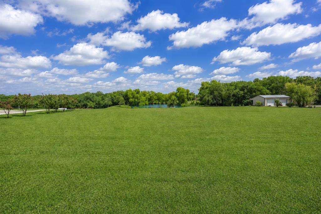 900 Hodgins Road Van Alstyne, TX 75495 - Photo 9 of 10 Expansive green space featuring a large metal building with multiple garage doors, mature trees, and a visible body of water