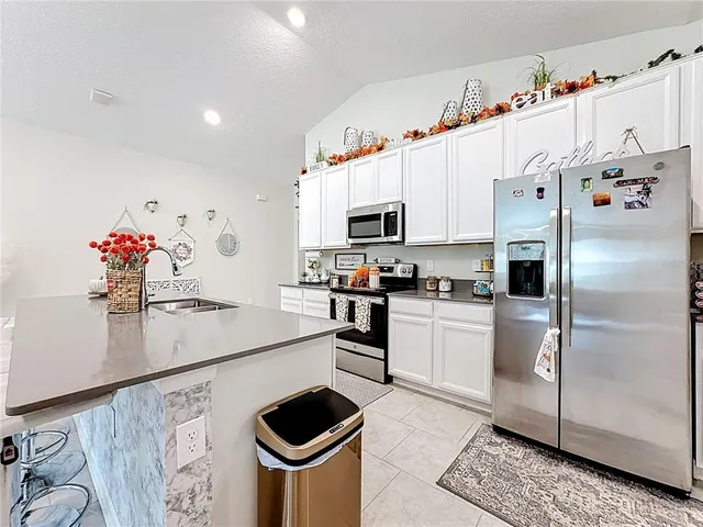 a white kitchen with stainless steel appliances granite countertop a refrigerator a stove a sink dishwasher and white cabinets with wooden floor
