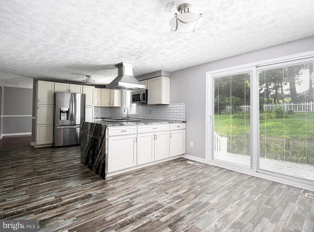 a kitchen with stainless steel appliances granite countertop a refrigerator a sink dishwasher a stove and a dining table with wooden floor