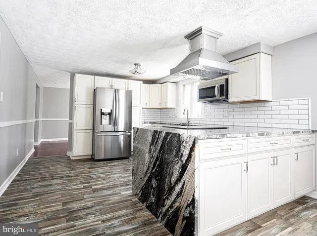 a kitchen with granite countertop a refrigerator a sink dishwasher a stove and white cabinets with wooden floor