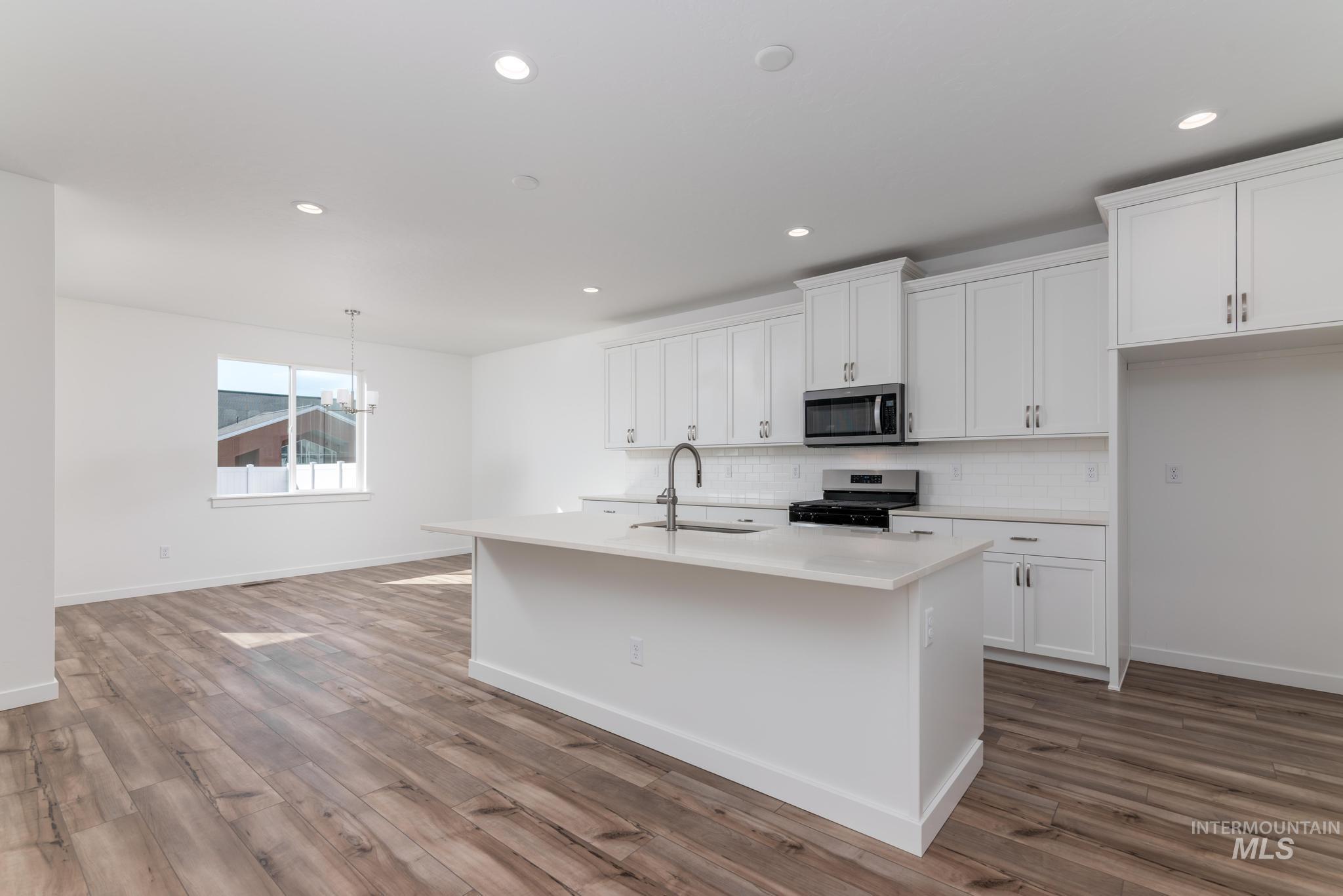 893 West Bay Street Middleton, ID 83644 - Photo 4 of 10 Kitchen featuring white cabinets, stainless steel appliances, an island with sink, a chandelier, and dark wood-style flooring