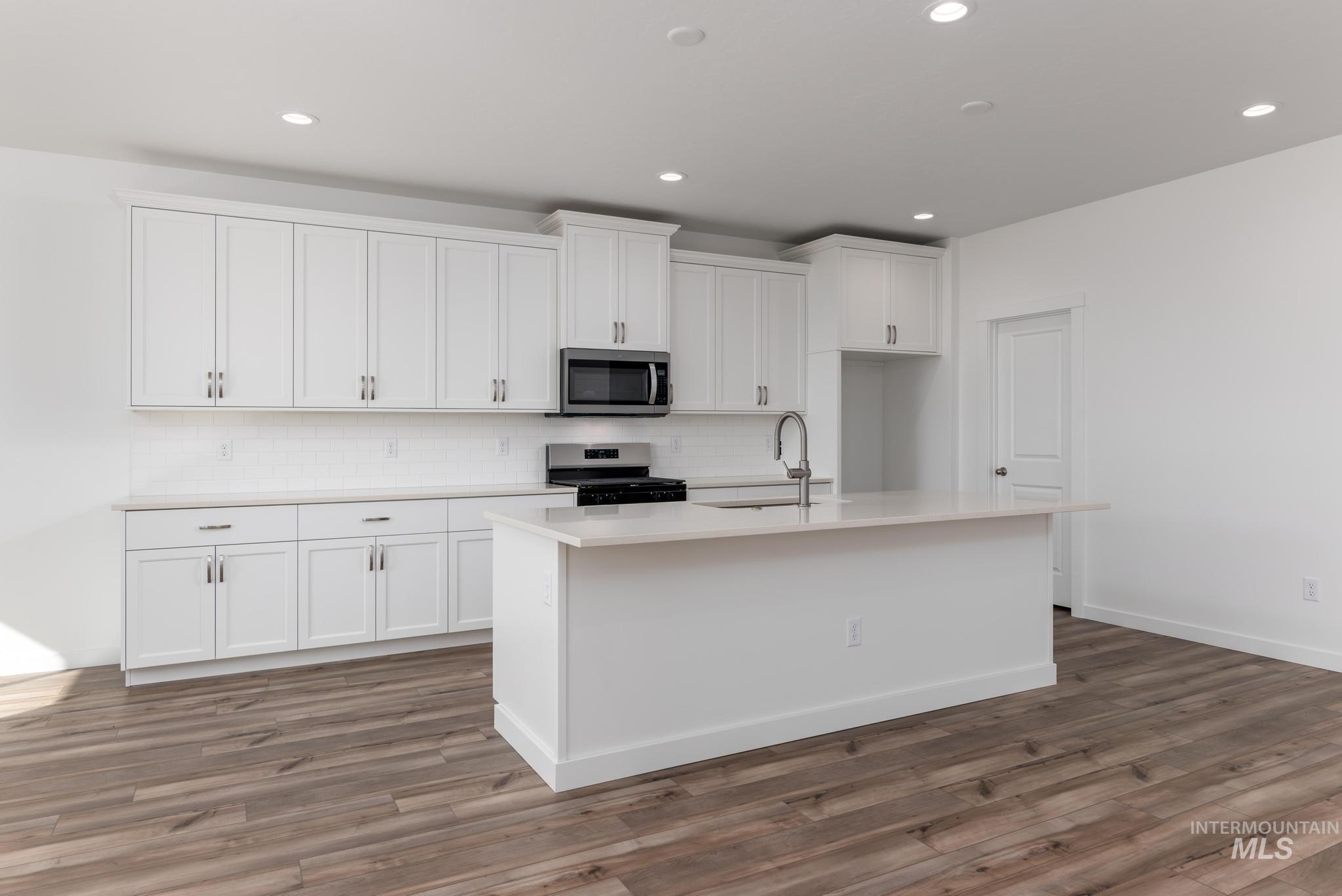 893 West Bay Street Middleton, ID 83644 - Photo 5 of 10 Kitchen with white cabinets, stainless steel appliances, decorative backsplash, a kitchen island with sink, and dark wood-type flooring