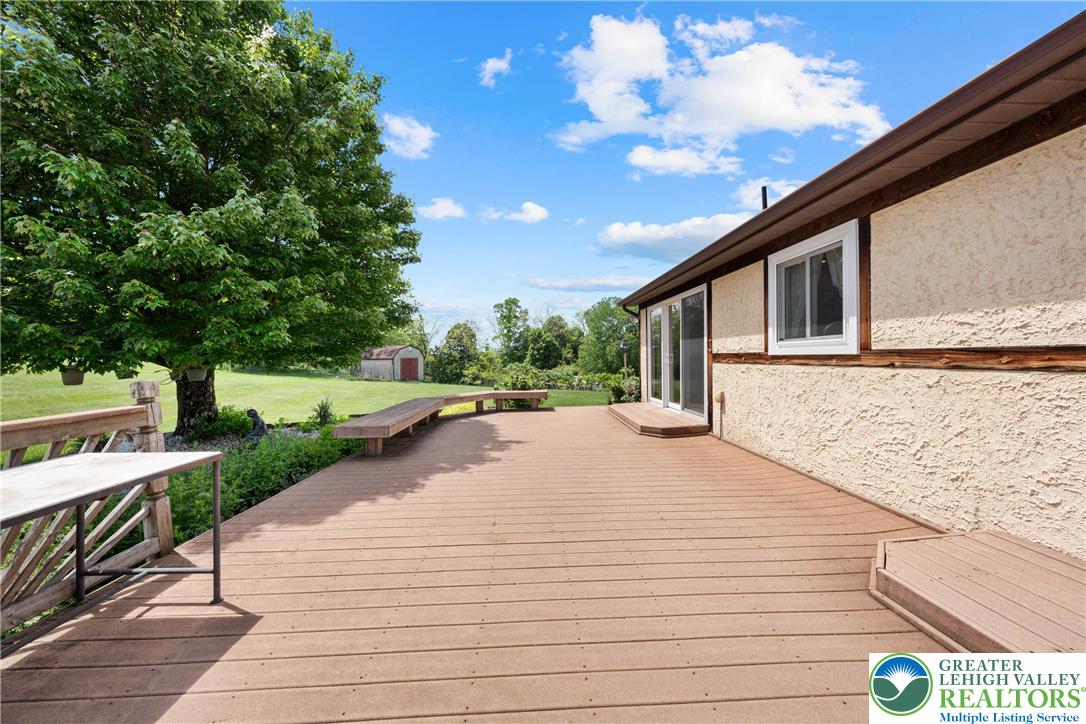 947 Tamenend Road Bath, PA 18014 - Photo 39 of 61 A spacious wooden deck extends from a stucco home, offering sweeping views of a verdant yard with mature trees.