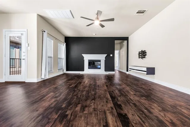 an empty room with wooden floor a ceiling fan a fireplace and windows