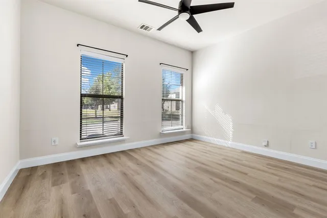 an empty room with wooden floor fan and windows
