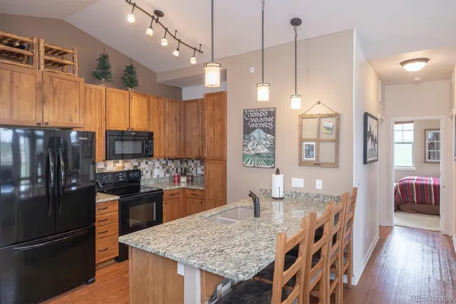 a kitchen with granite countertop a refrigerator a stove a sink dishwasher a kitchen island with wooden cabinets and floor