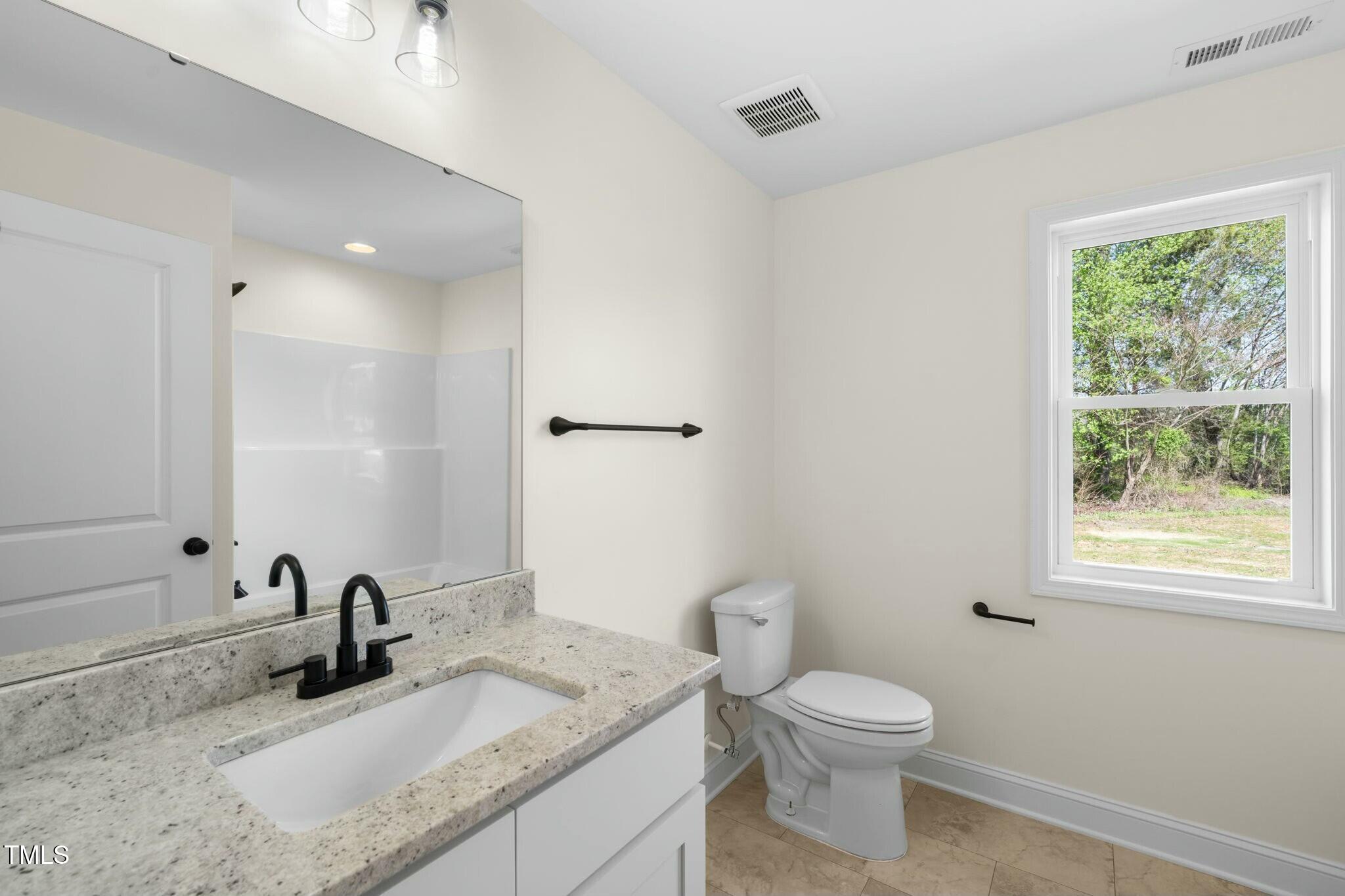8917 Fowler Road Zebulon, NC 27597 - Photo 15 of 33 a bathroom with a granite countertop toilet a sink and a mirror
