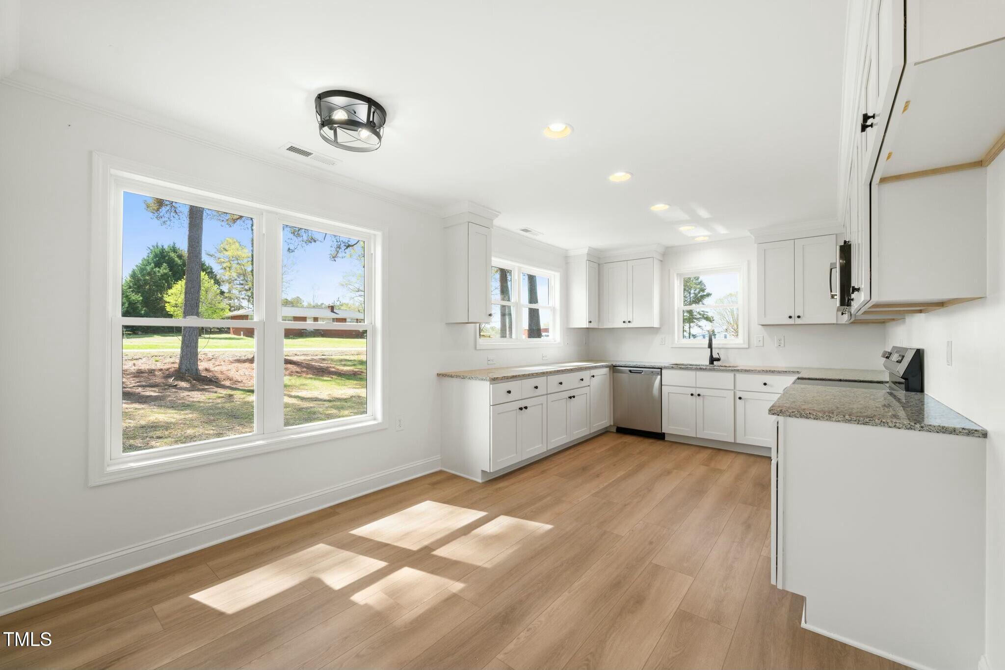 8917 Fowler Road Zebulon, NC 27597 - Photo 23 of 33 a kitchen with stainless steel appliances granite countertop a stove a sink dishwasher and white cabinets with wooden floor