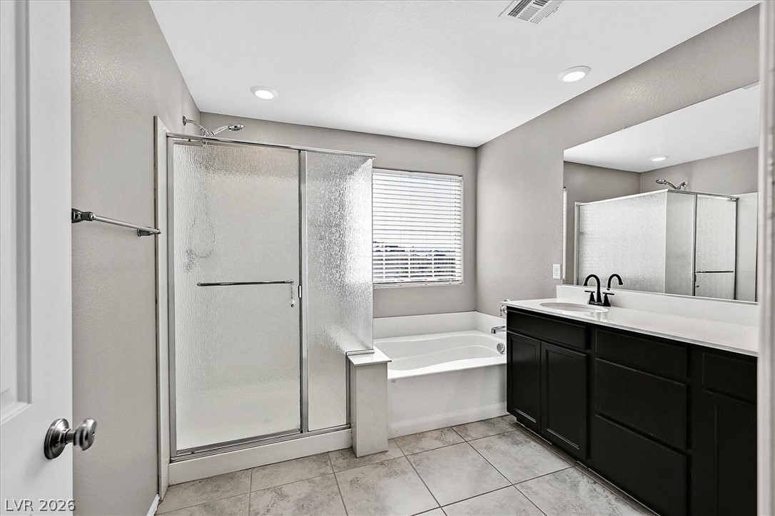 2823 Turnstone Ridge Street Henderson, NV 89044 - Photo 12 of 25 A well-lit bathroom featuring a tub, a walk-in shower, and a wide vanity with ample storage.