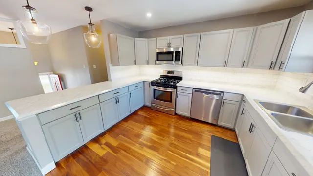 a kitchen with stainless steel appliances granite countertop a sink a stove top oven a refrigerator with white cabinets and wooden floor