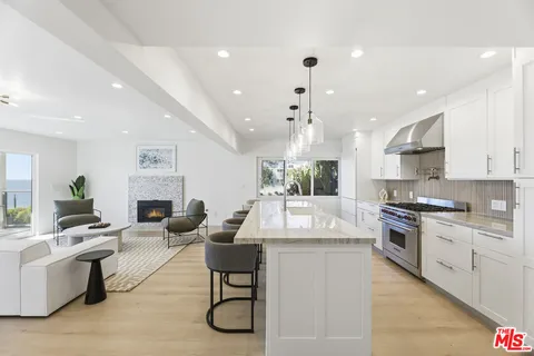 a large white kitchen with granite countertop a stove a sink a refrigerator and white cabinets with wooden floor