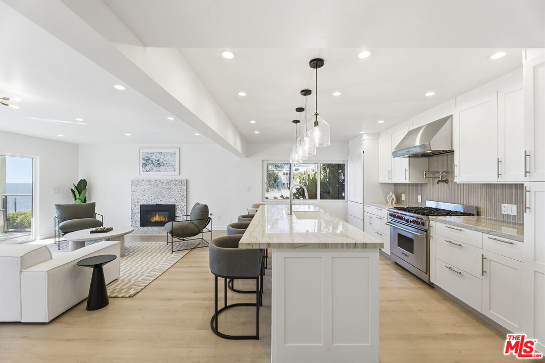 2442 South Coast Highway, Unit 3 Laguna Beach, CA 92651 - Photo 4 of 30 a large white kitchen with granite countertop a stove a sink a refrigerator and white cabinets with wooden floor
