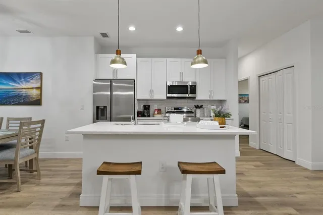 a kitchen with stainless steel appliances granite countertop a sink a stove a refrigerator and a dining table with wooden floor