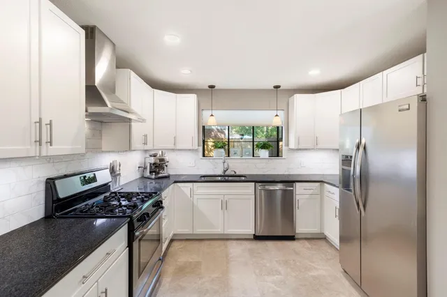 a kitchen with stainless steel appliances granite countertop a sink stove refrigerator and cabinets
