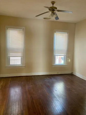 a view of a livingroom with wooden floor a ceiling fan and windows