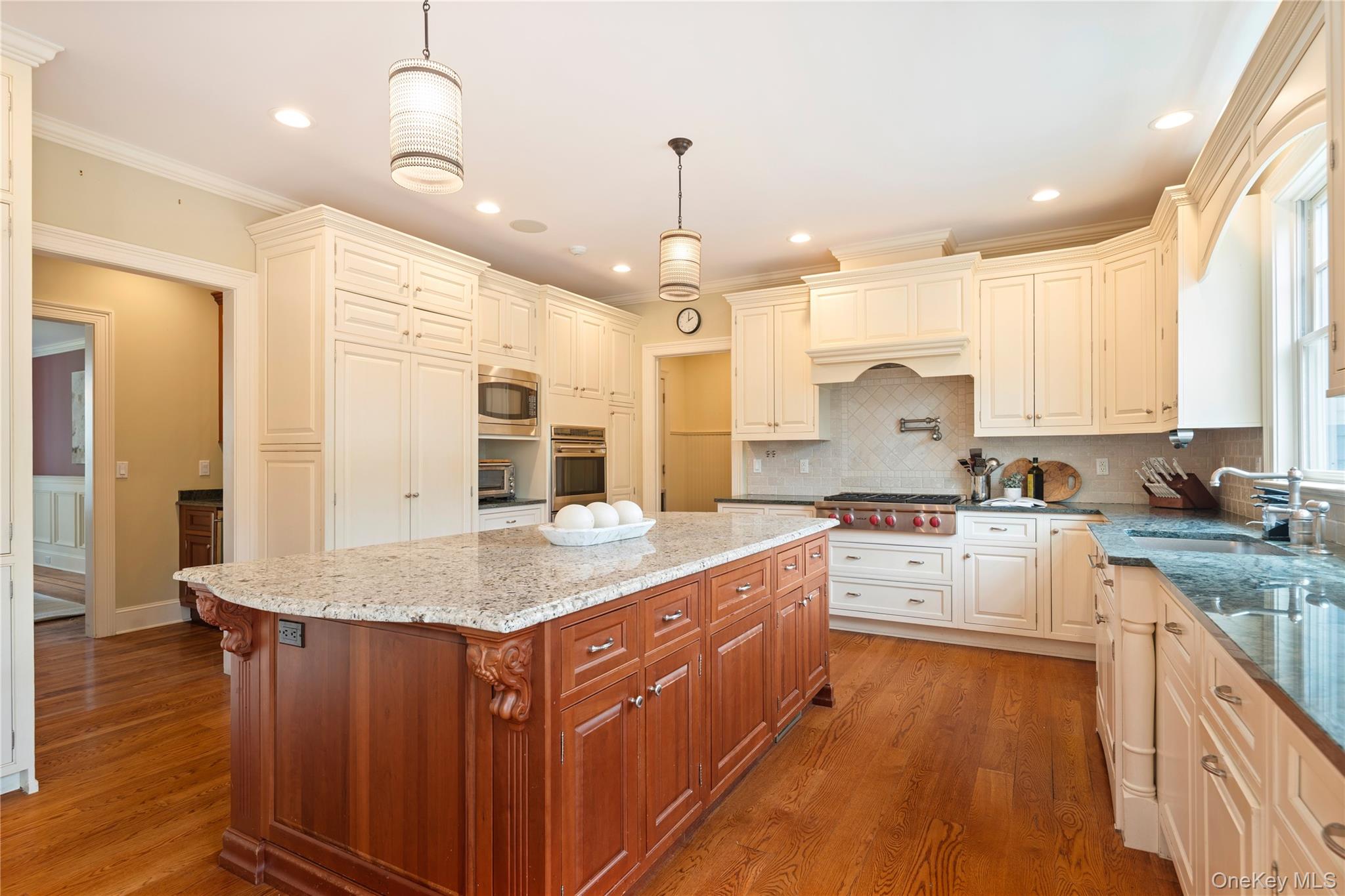 77 Byram Ridge Road Armonk, NY 10504 - Photo 21 of 48 Kitchen with custom soft close cabinetry, large center island with seating and granite counters, Subzero with integral door panels, tumbled marble backsplash, Wolf stainless steel gas 6 burner cooktop, pot filler above, Wolf stainless steel double convection wall ovens, built-in microwave, 2 Bosch dishwashers with integral door panels, recessed LED lighting, wide board oak floors, pendant lighting, large window overlooking back yard, door to butlers pantry, mud room