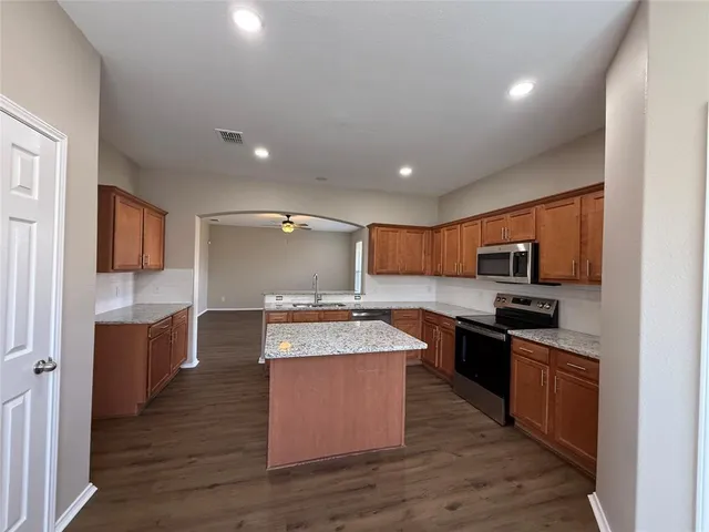 a kitchen with stainless steel appliances granite countertop a stove top oven a sink dishwasher a refrigerator and a dining table with wooden floor