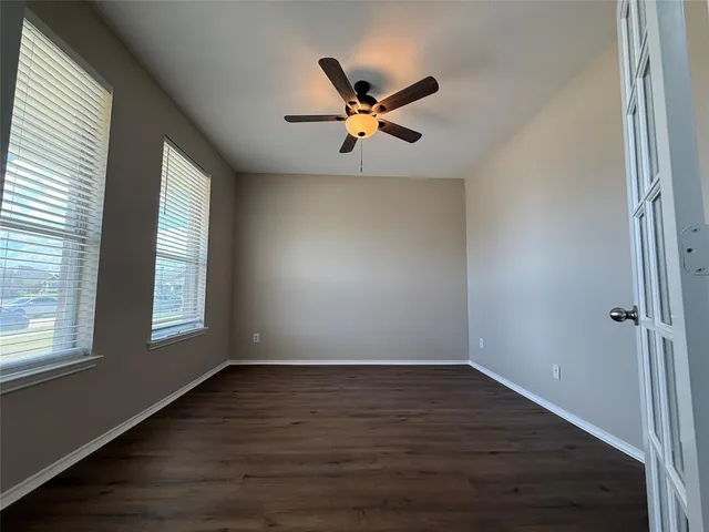 an empty room with wooden floor fan and windows