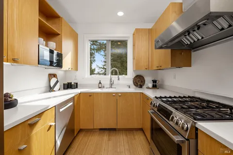 a kitchen with stainless steel appliances a refrigerator a sink a stove and white cabinets with wooden floor