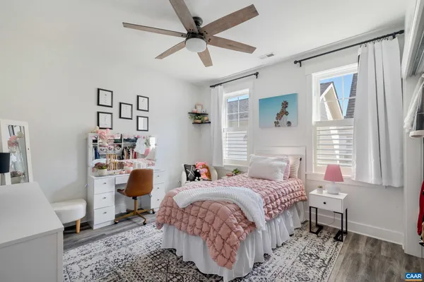 a bedroom with a bed a desk and chair with wooden floor
