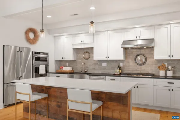 a kitchen with stainless steel appliances granite countertop a sink a stove a refrigerator and chairs