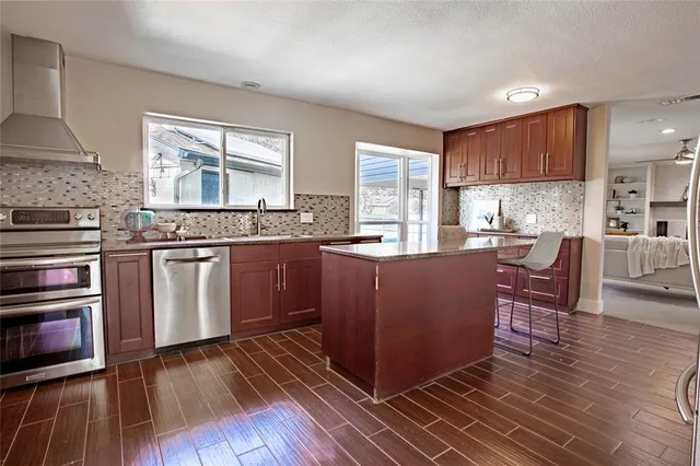 a kitchen with stainless steel appliances granite countertop wooden cabinets a sink a stove a dining table and chairs