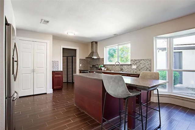 a kitchen with stainless steel appliances granite countertop a stove a refrigerator a sink a dining table and chairs with wooden floor