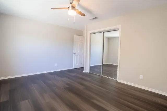 an empty room with wooden floor fan and windows