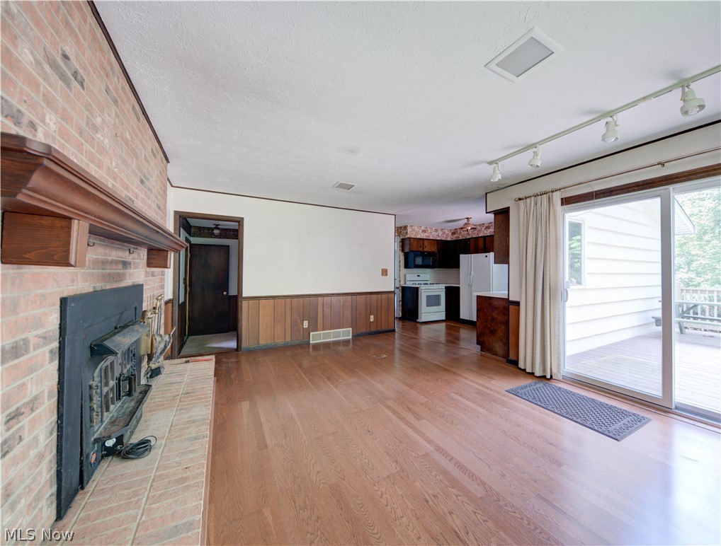 11430 Ferry Road Chesterland, OH 44026 - Photo 12 of 38 Unfurnished living room with a fireplace, light wood-type flooring, track lighting, a wood stove, and brick wall
