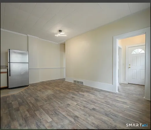a view of an empty room with wooden floor and a kitchen