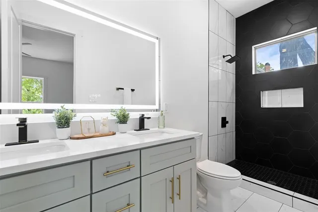 a bathroom with a granite countertop sink a toilet a mirror and shower