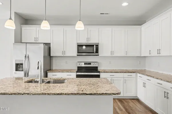 a kitchen with stainless steel appliances granite countertop a sink a stove a refrigerator and white cabinets