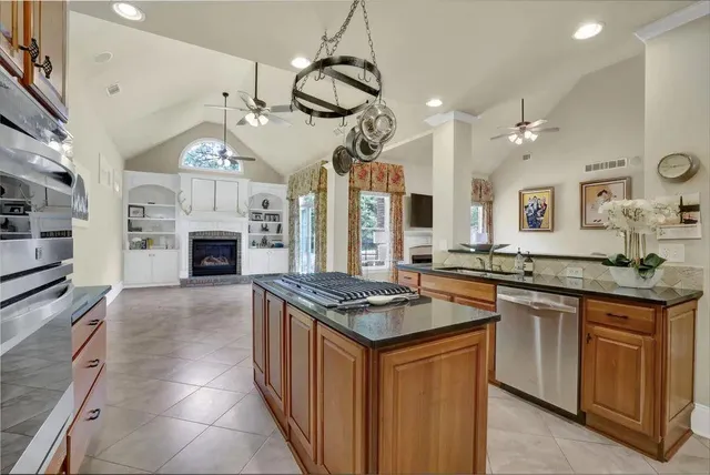 a kitchen with stainless steel appliances granite countertop a stove a sink dishwasher a refrigerator and a fireplace with wooden floor