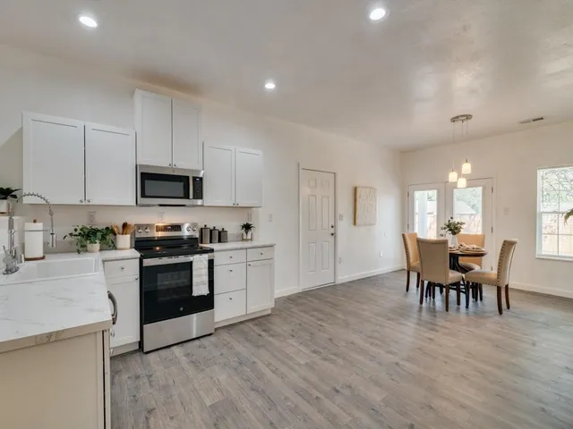 a kitchen with stainless steel appliances granite countertop a stove top oven a sink dishwasher a dining table and chairs with wooden floor