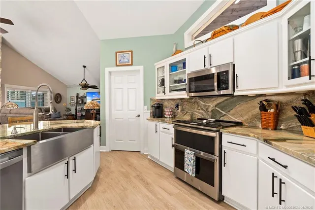 a kitchen with stainless steel appliances granite countertop a stove top oven a sink a refrigerator white cabinets and wooden floor