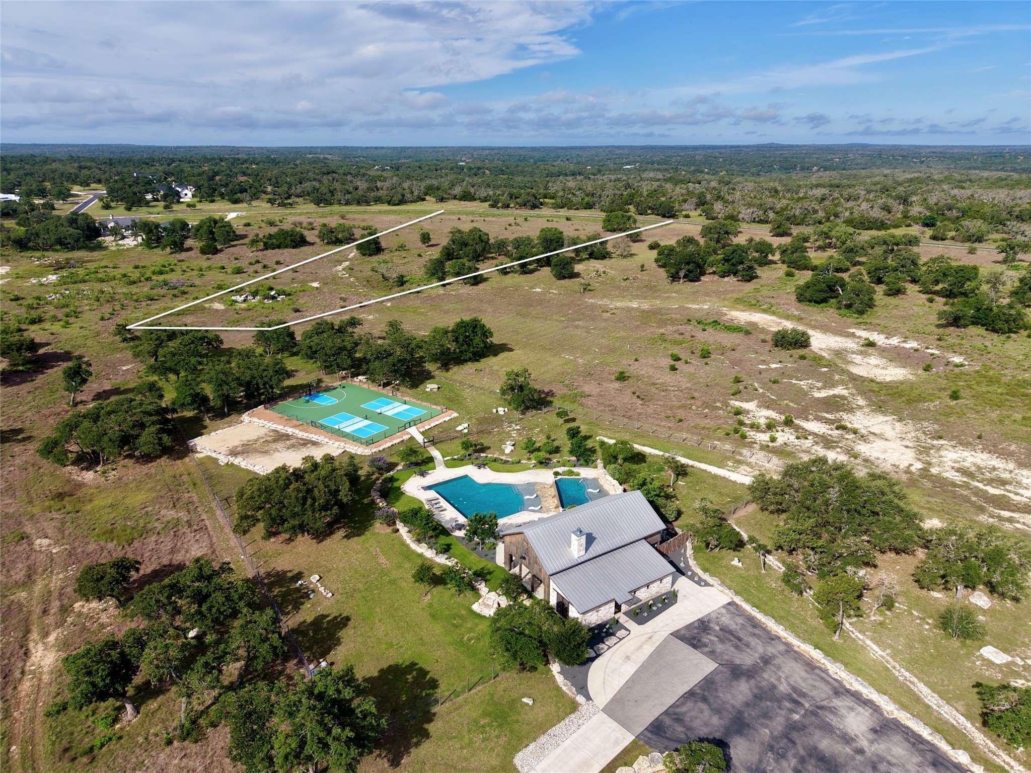 485 Inspiration Loop Comfort, TX 78013 - Photo 14 of 22 An aerial panorama reveals a private estate featuring a contemporary residence, inviting pool, and multi-sport court set amidst sprawling natural landscape.