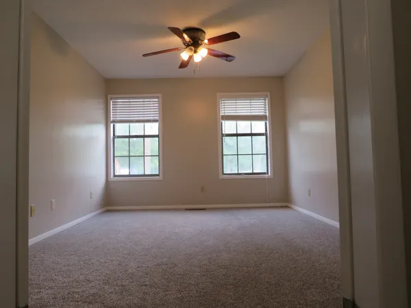 an empty room with ceiling fan and windows