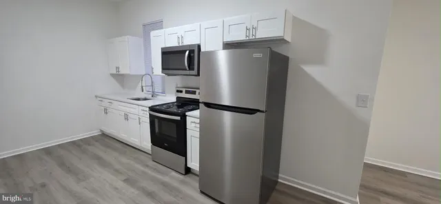a kitchen with stainless steel appliances a refrigerator a sink and white cabinets