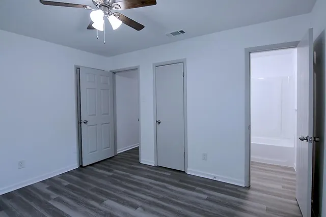an empty room with wooden floor closet and windows