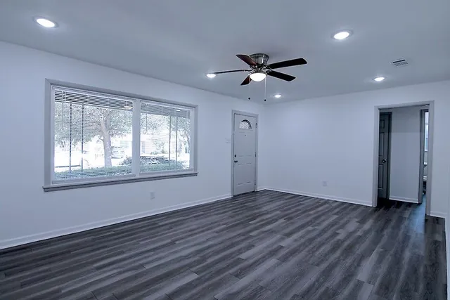 a view of an empty room with wooden floor and a window