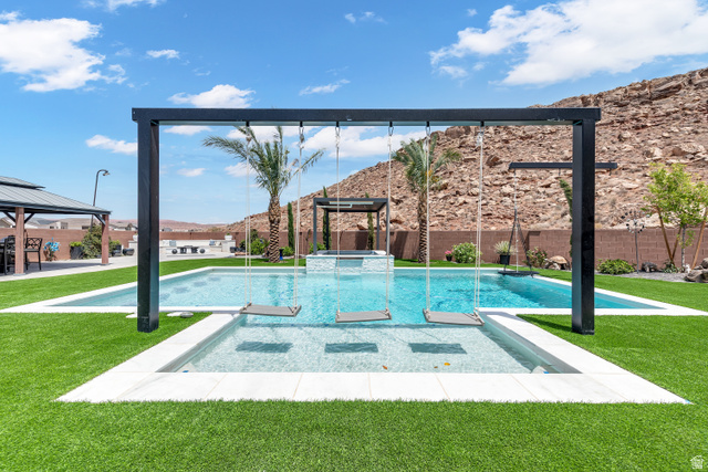 6105 Bunda Way St. George, UT 84790 - Photo 39 of 49 Resort-style pool area featuring a tanning ledge with built-in swings, artificial turf landscaping, and a separate elevated spa