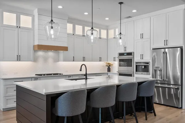 a kitchen with stainless steel appliances granite countertop a sink a stove a refrigerator and chairs