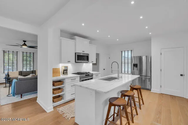 a open kitchen with stainless steel appliances kitchen island granite countertop a stove top oven a sink dishwasher and white cabinets with wooden floor