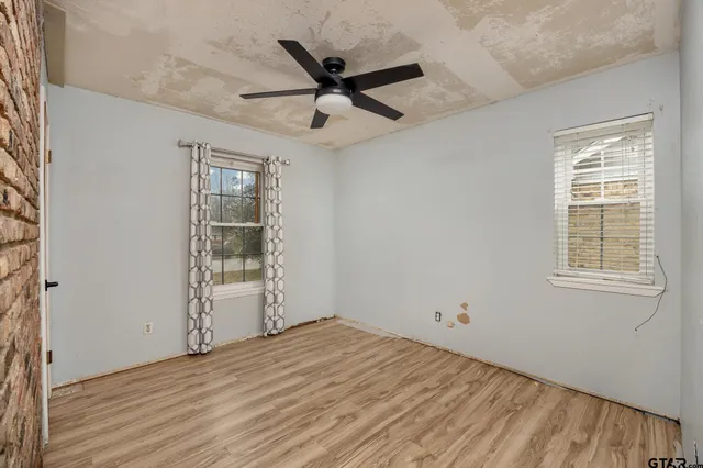 an empty room with wooden floor fan and windows