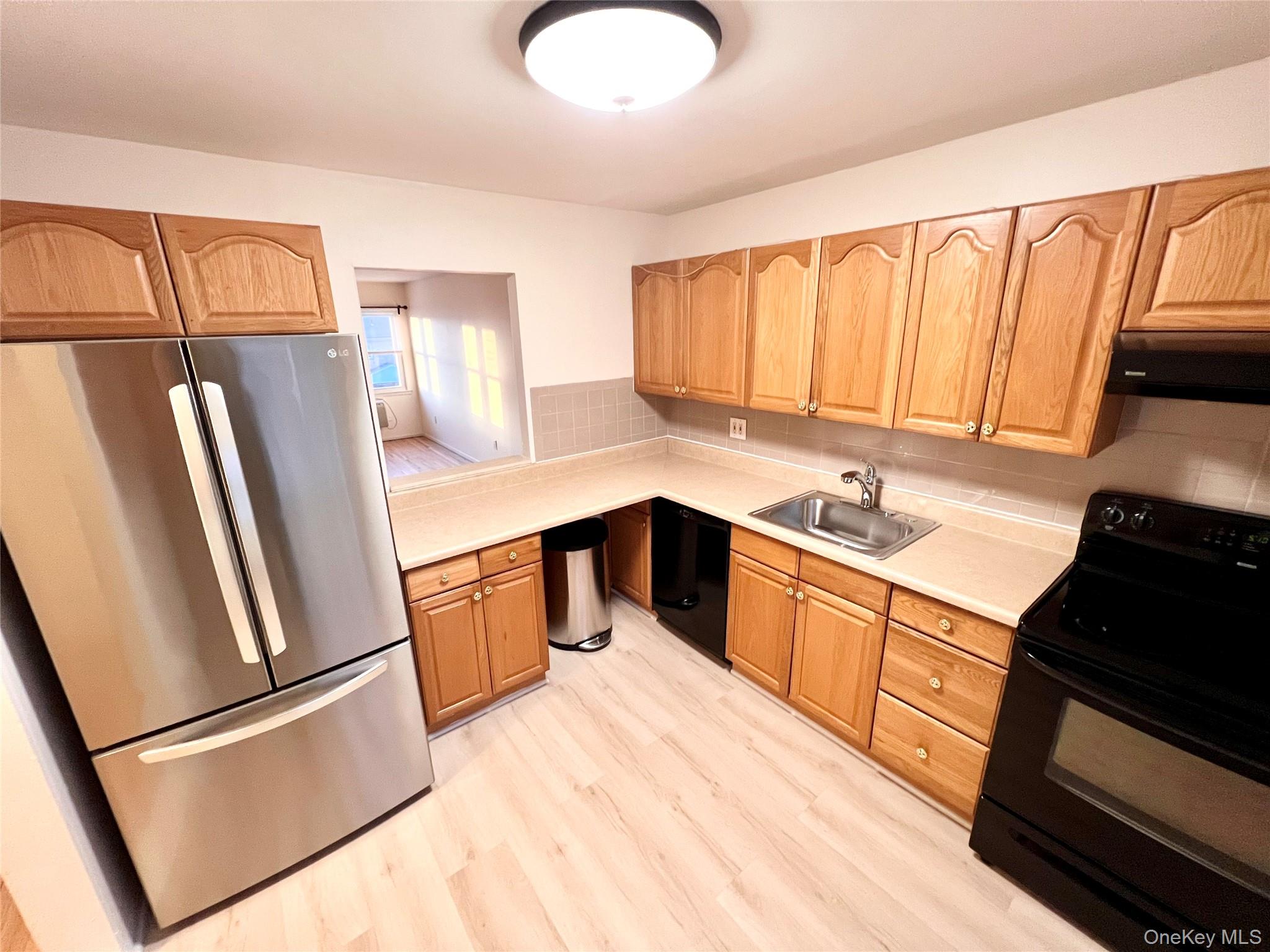 Kitchen with black appliances, light countertops, exhaust hood, light wood-style floors, and tasteful backsplash