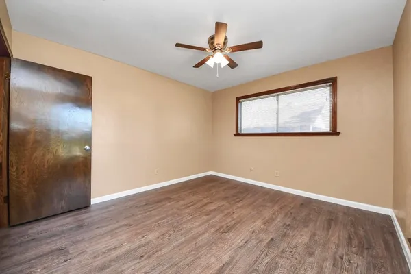 a view of an empty room with wooden floor and a ceiling fan
