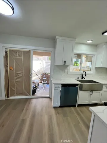 a open kitchen with granite countertop a stove a sink a refrigerator and white cabinets with wooden floor