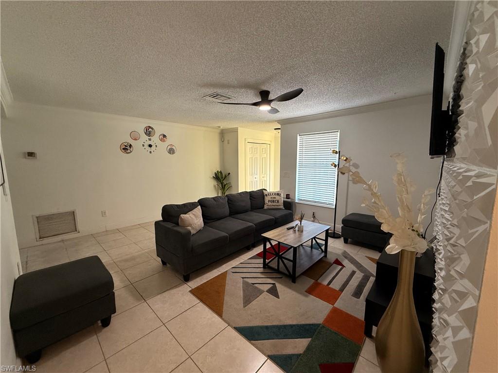 3536 Bolero Way Naples, FL 34105 - Photo 16 of 25 Living area featuring light tile patterned floors, a textured ceiling, a ceiling fan, and crown molding
