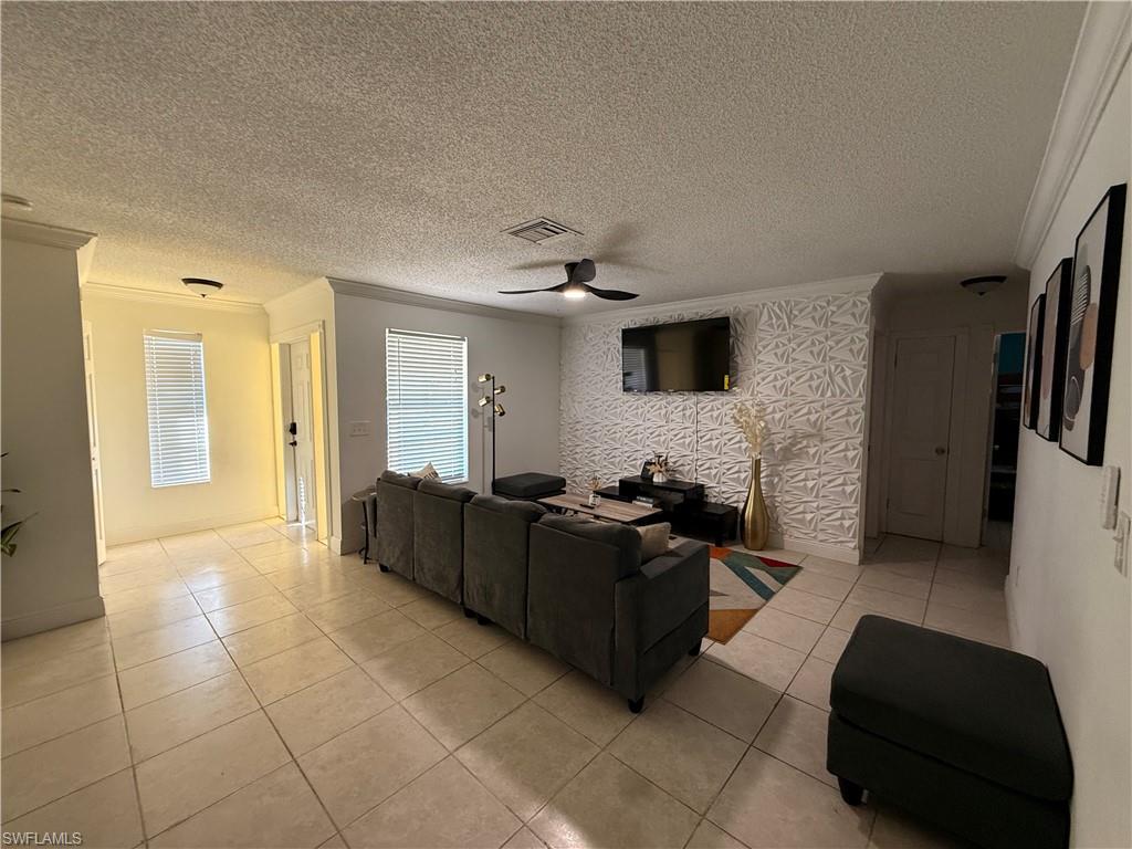 3536 Bolero Way Naples, FL 34105 - Photo 17 of 25 Living area featuring a textured ceiling, crown molding, light tile patterned floors, a ceiling fan, and an accent wall