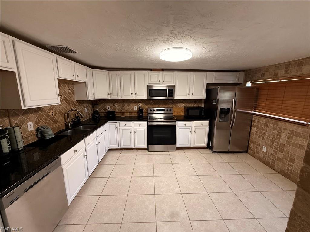 3536 Bolero Way Naples, FL 34105 - Photo 19 of 25 Kitchen with stainless steel appliances, white cabinetry, a textured ceiling, light tile patterned floors, and dark stone counters